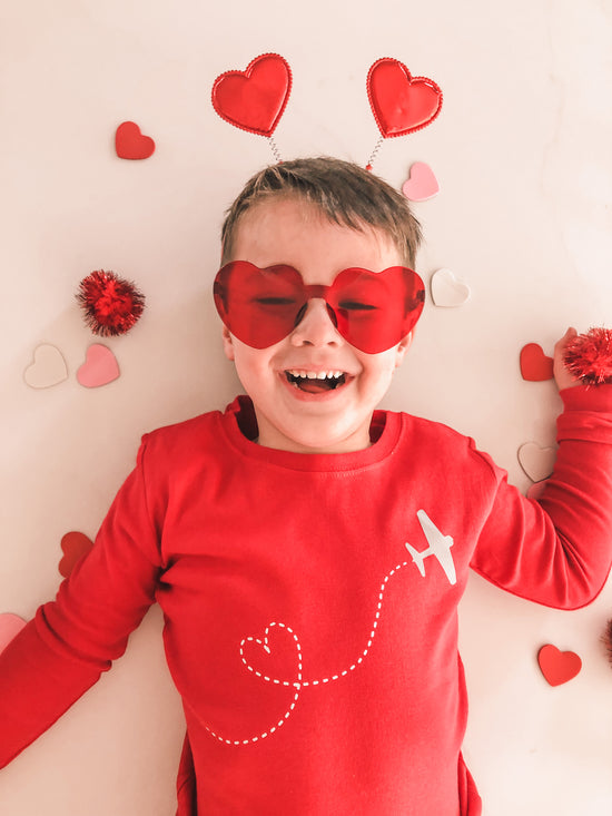 boy with valentine stickers and hearts around him with heart sunglasses and headband, smiling